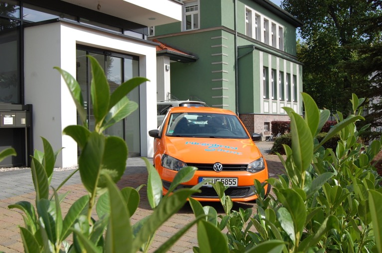 Das grün-weiße Gebäude des Pflegedienstes Sonne mit dem orangen Dienstwagen davor